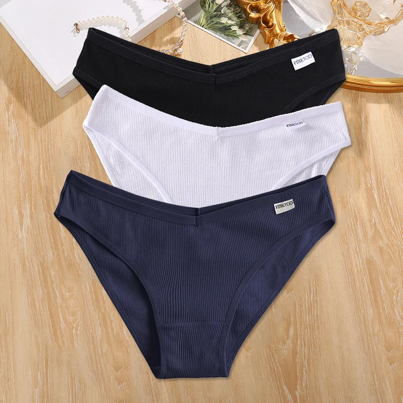 Three pairs of underwear in black, white, and navy on a wooden surface.