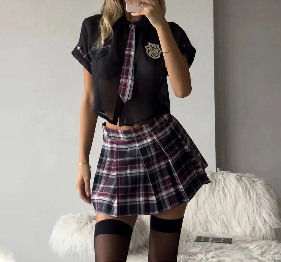 Person wearing a black shirt with a plaid tie and skirt, standing in a room.