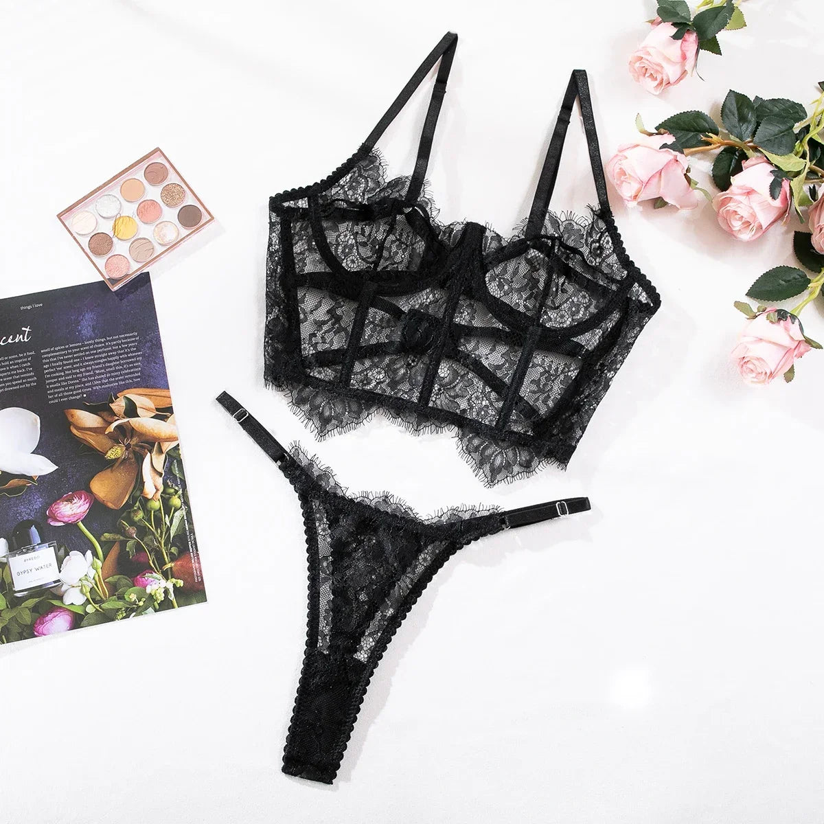 Black lace lingerie set on a white surface with flowers and a magazine.