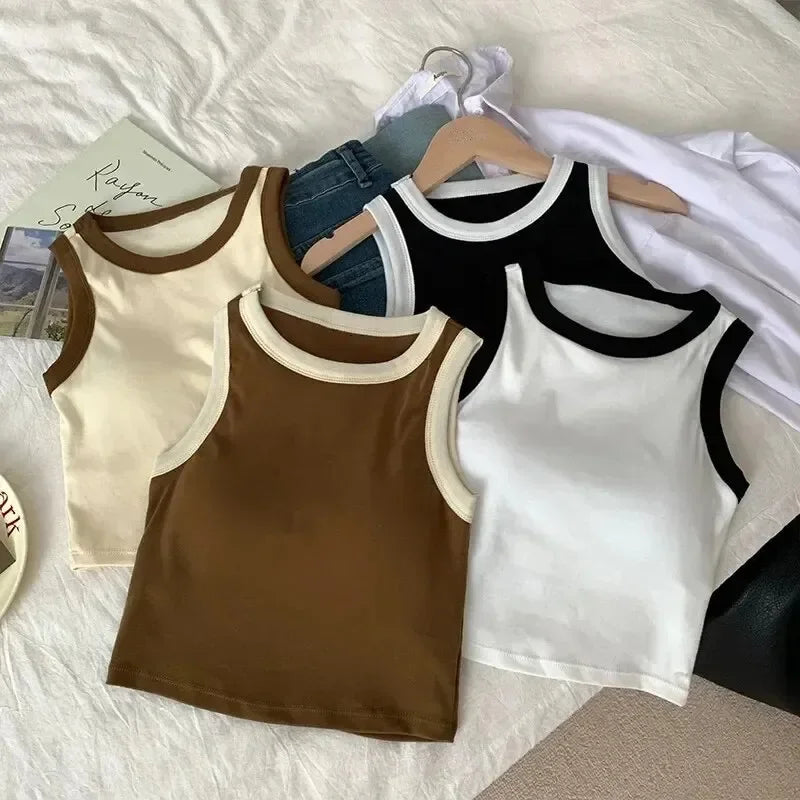 Four tank tops in beige, brown, black, and white on hangers against a light background.