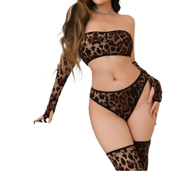A woman modeling a leopard-print lingerie set with a long-sleeve bandeau top, matching high-cut bottoms, and thigh-high stockings against a plain white background.