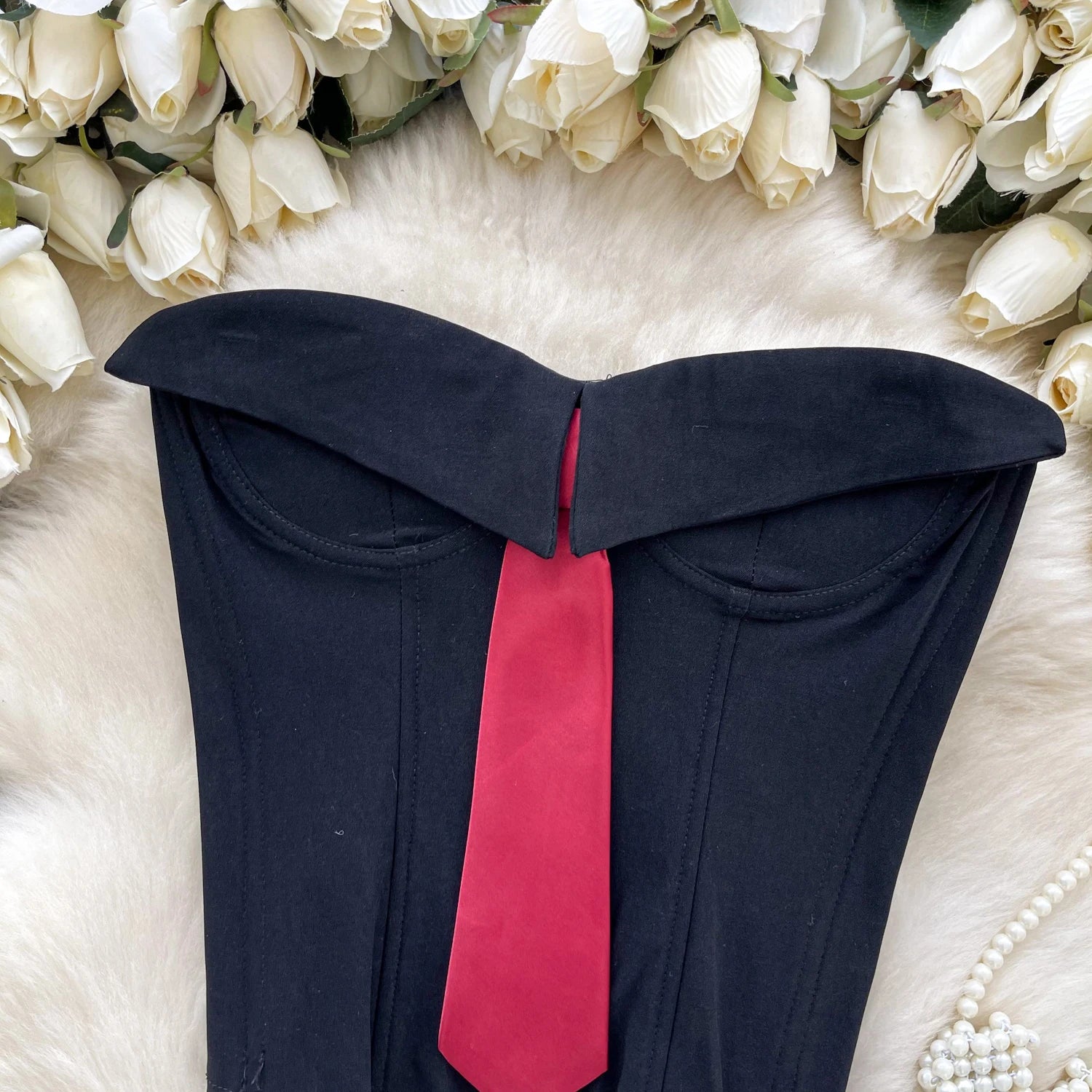 Black strapless top with a red tie on a white fur surface with white roses in the background