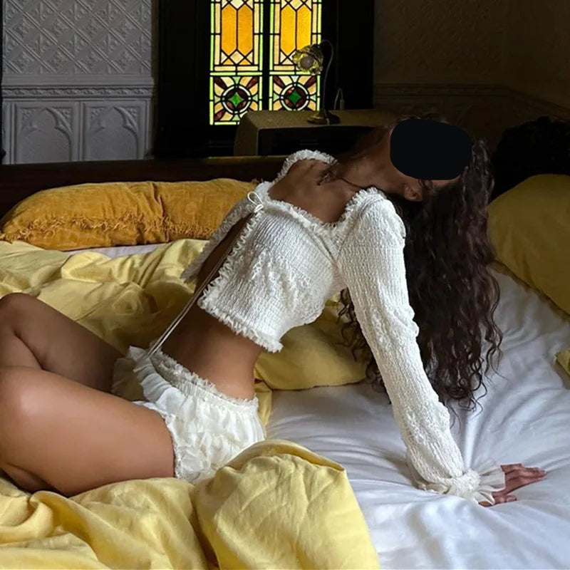 Woman in a white outfit lying on a bed with yellow bedding and stained glass window in the background.