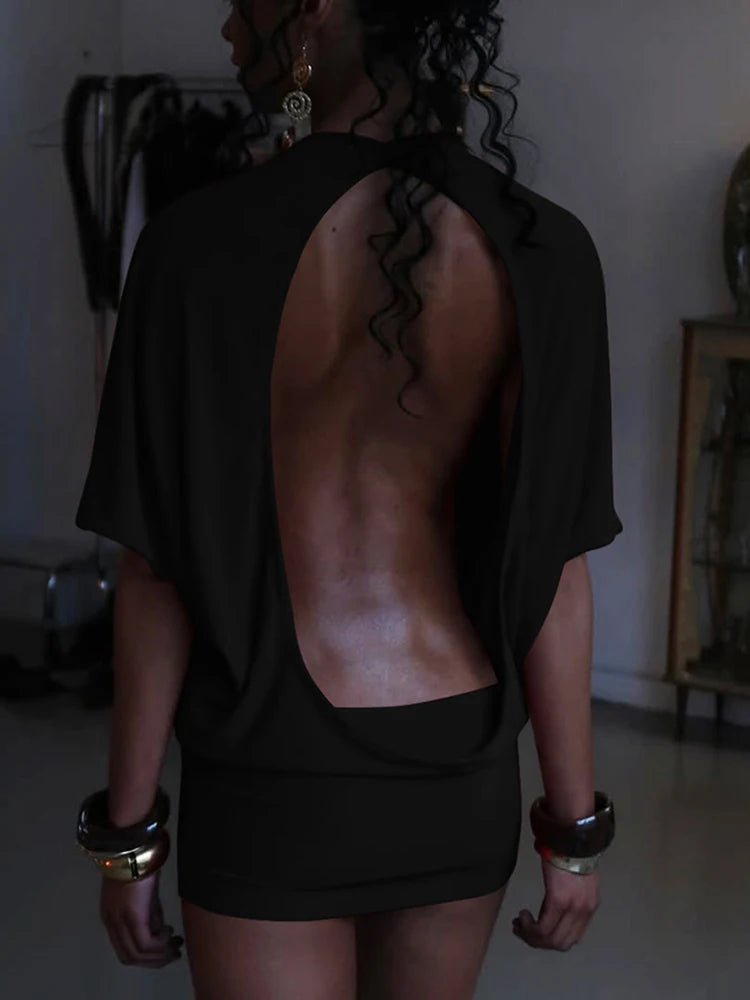 Person wearing a black open-back top and shorts in an indoor setting