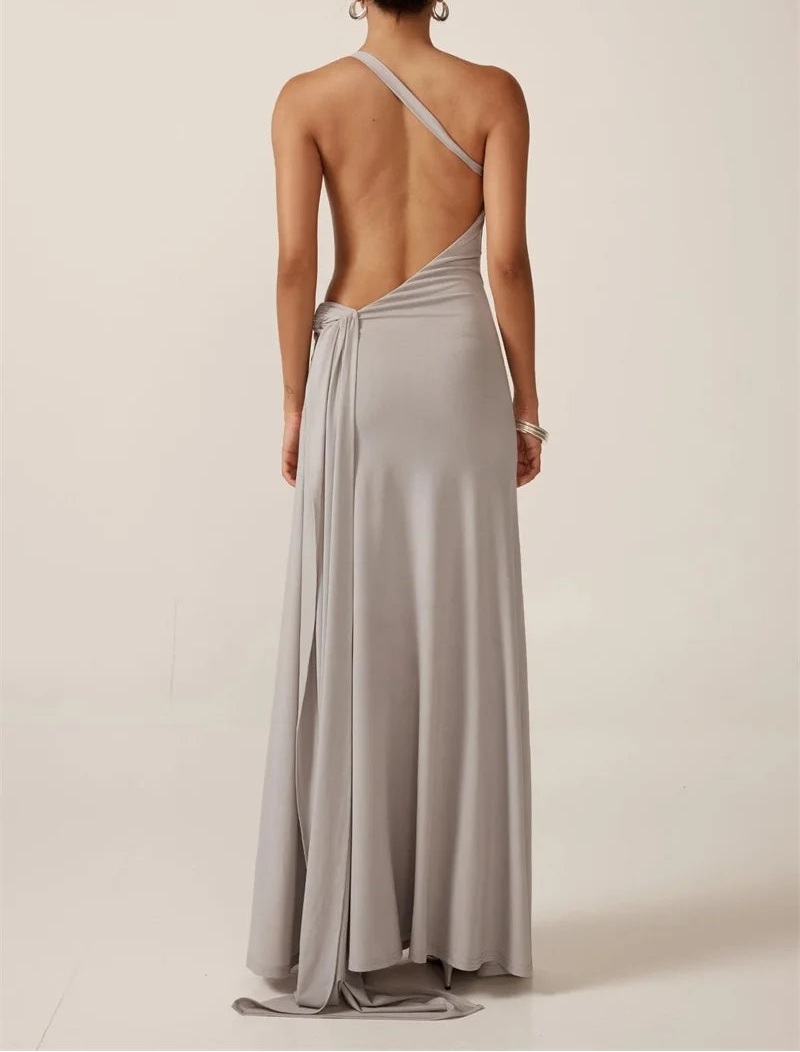 Woman wearing a long, light gray dress with a backless design on a plain background