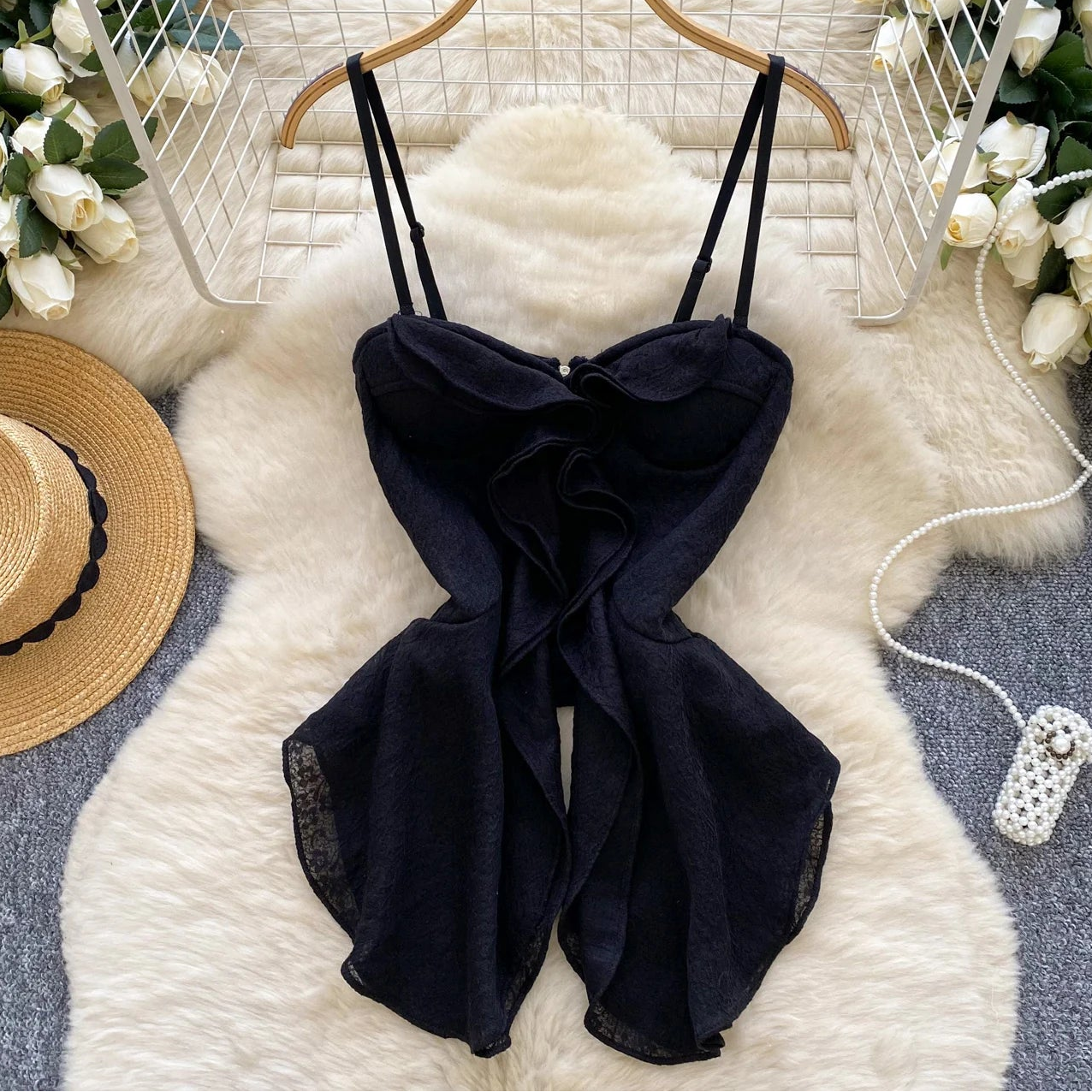 Black dress on a hanger with flowers and a hat in the background
