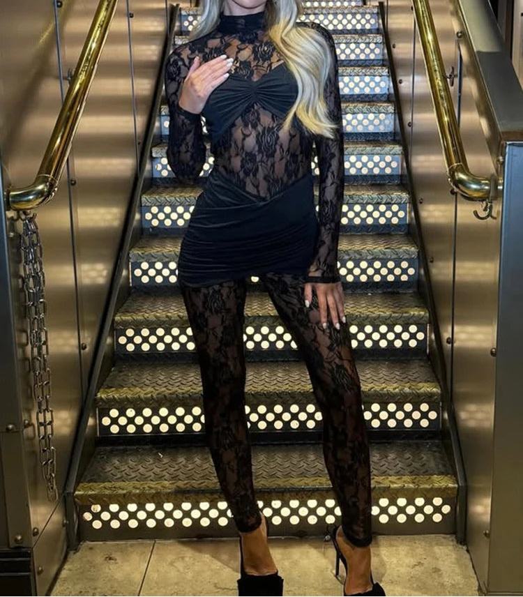 Woman in a black lace outfit standing on a staircase with decorative railings.