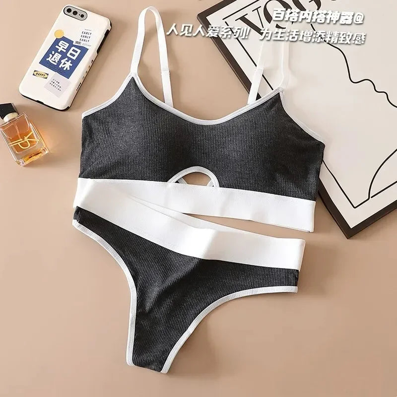 Black and white bikini set on a beige surface with a phone, perfume bottle, and box in the background.