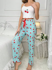 Woman wearing a white crop top with cherry design and light blue pants with red cherry pattern in a bedroom setting.