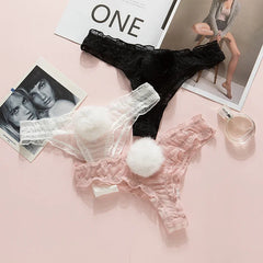 Black lace bra and panties with white pom-poms on a pink surface with magazines.