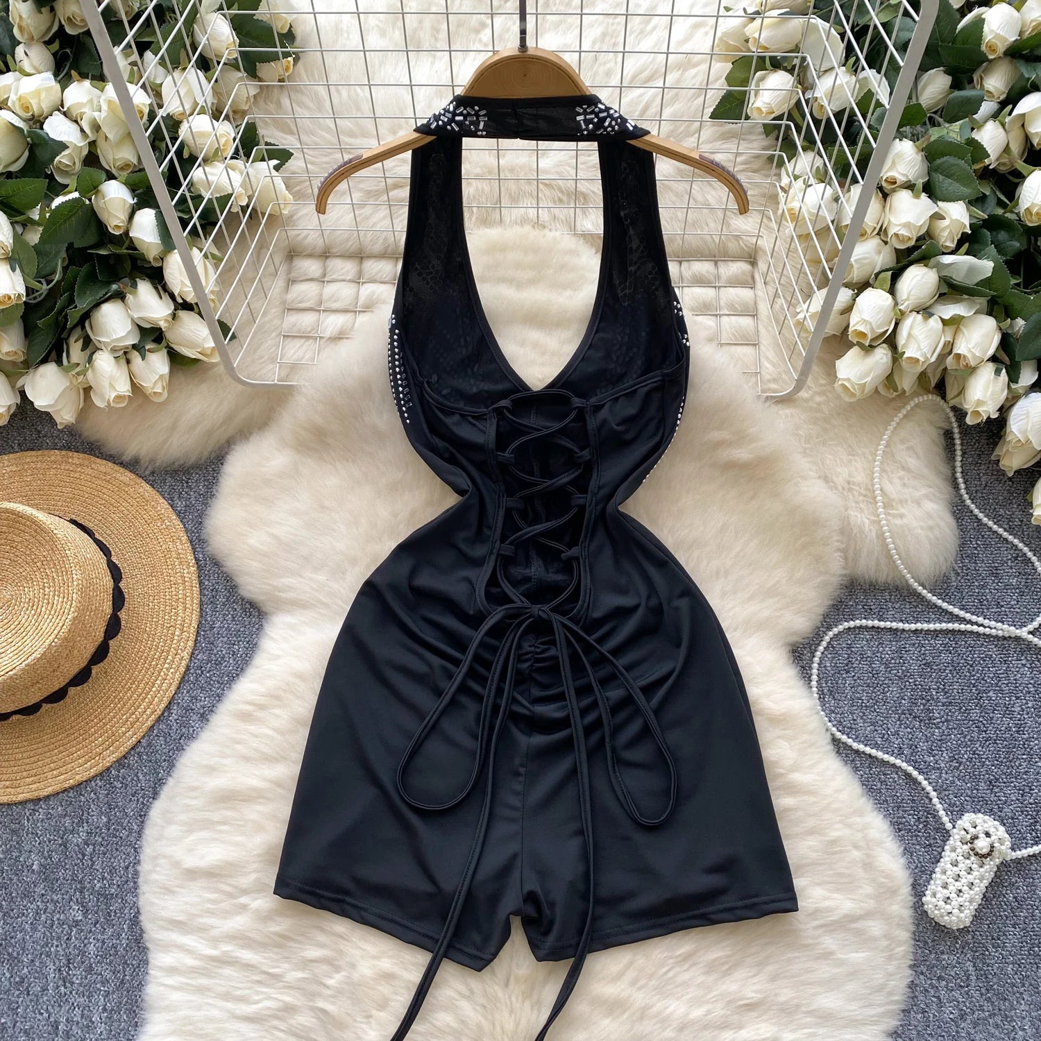 Black halter-style romper on a hanger with decorative elements and flowers in the background