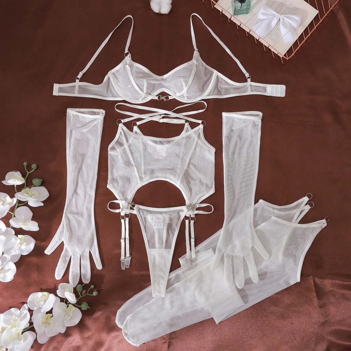 White lingerie set with gloves and stockings on a brown surface with flowers.