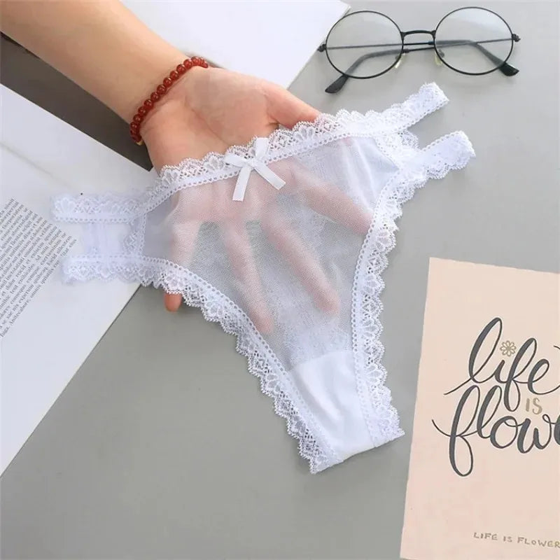 White lace-trimmed underwear held by a hand on a gray surface with glasses and a book.