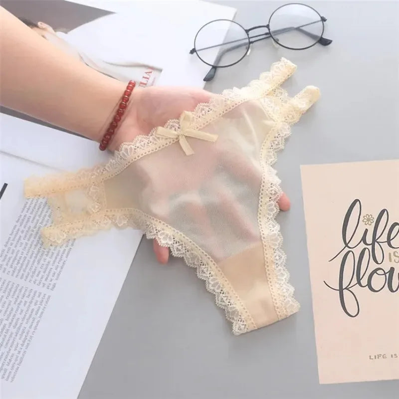Beige lace gloves held by a hand on a light gray surface with glasses and a book in the background.