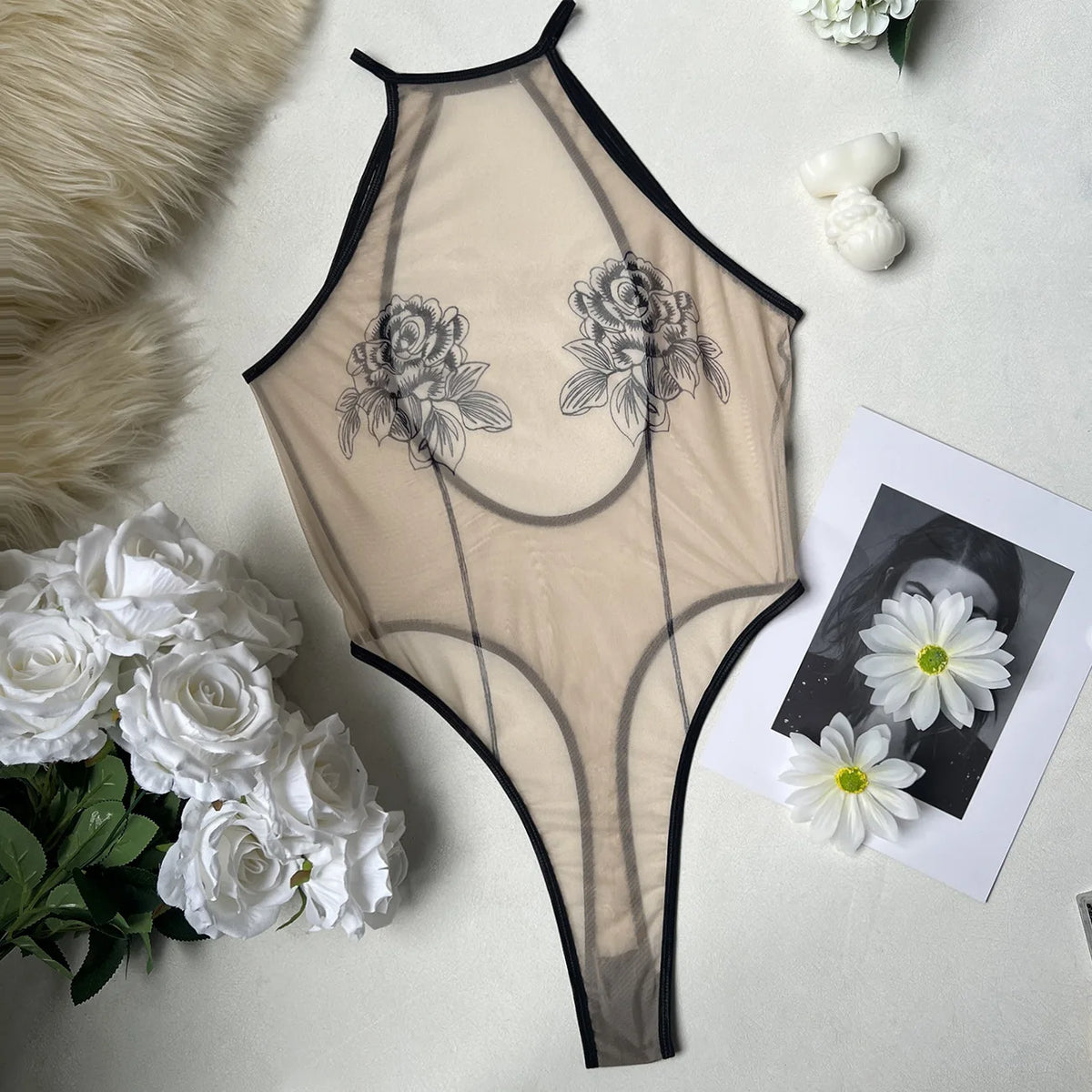 Beige bodysuit with floral designs on a white surface with flowers and a photo.