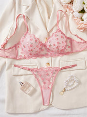 Pink floral lingerie set on a white surface with a jacket and flowers.