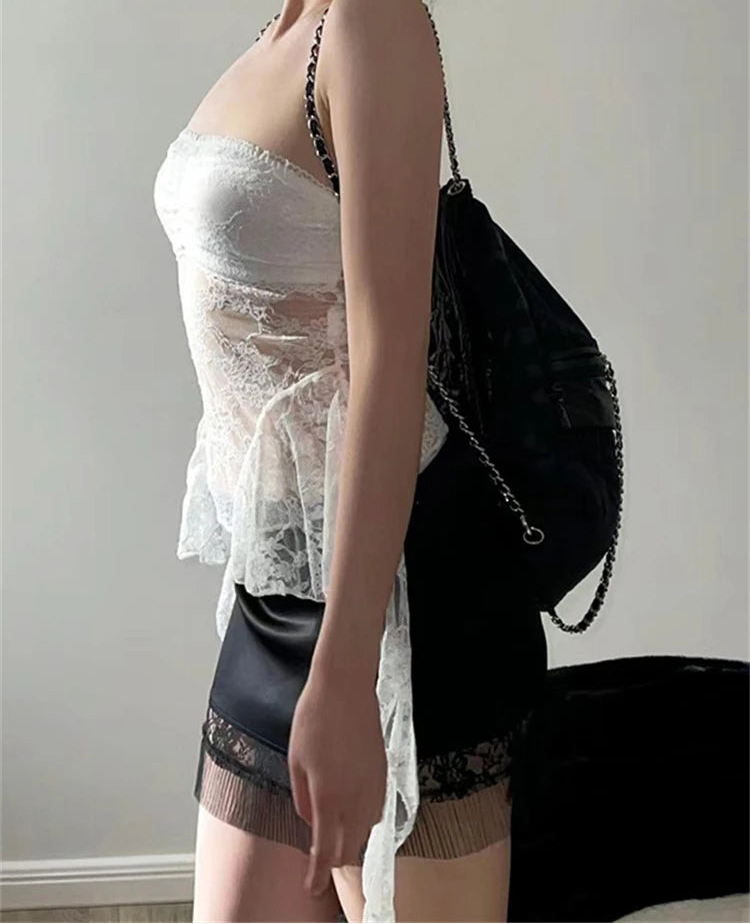 Person wearing a sheer white top and black shorts with a black bag on a plain background