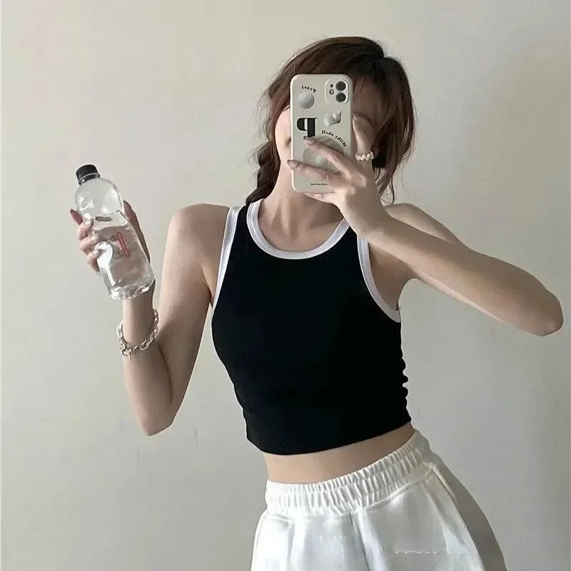 Person taking a mirror selfie wearing a black tank top and white pants, holding a water bottle.
