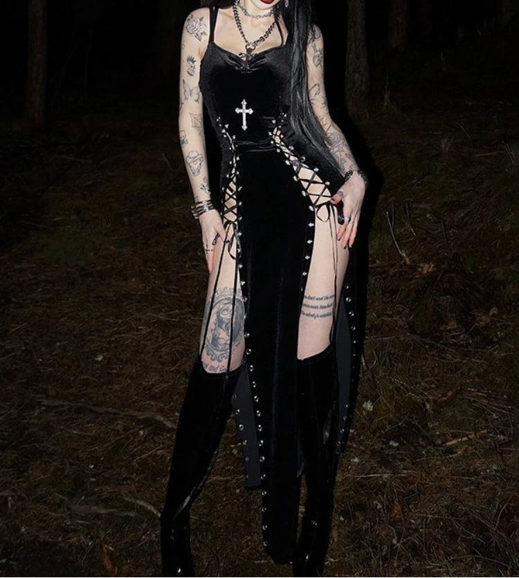 Person wearing a black gothic outfit with tattoos standing in a dark forest.