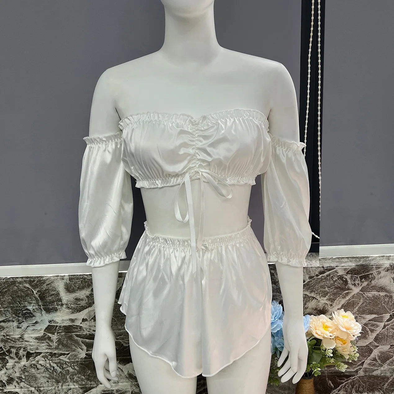 Mannequin wearing a white satin outfit with sheer sleeves against a gray background.