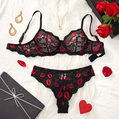 Black lace lingerie set with red accents on a white surface, surrounded by jewelry and flowers.
