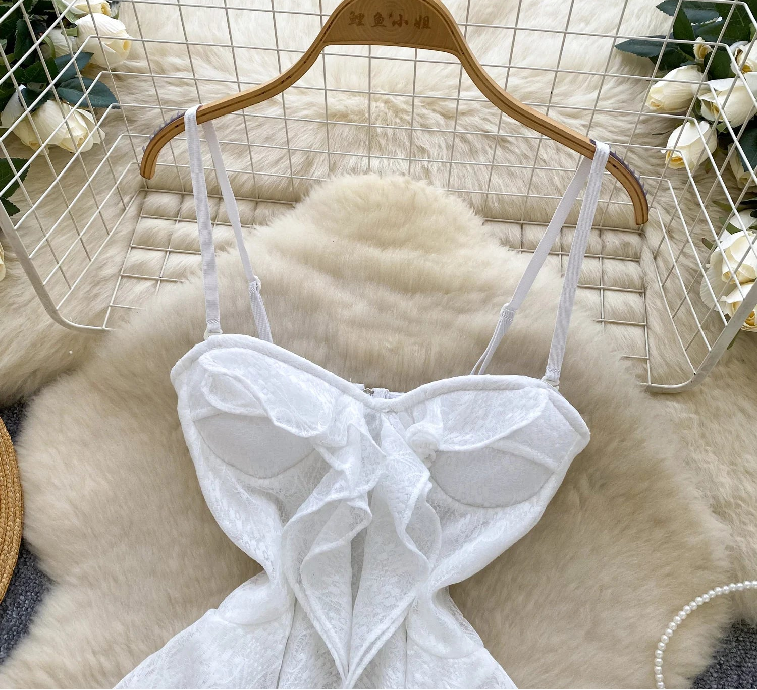 White lace top on a wooden hanger against a textured white background