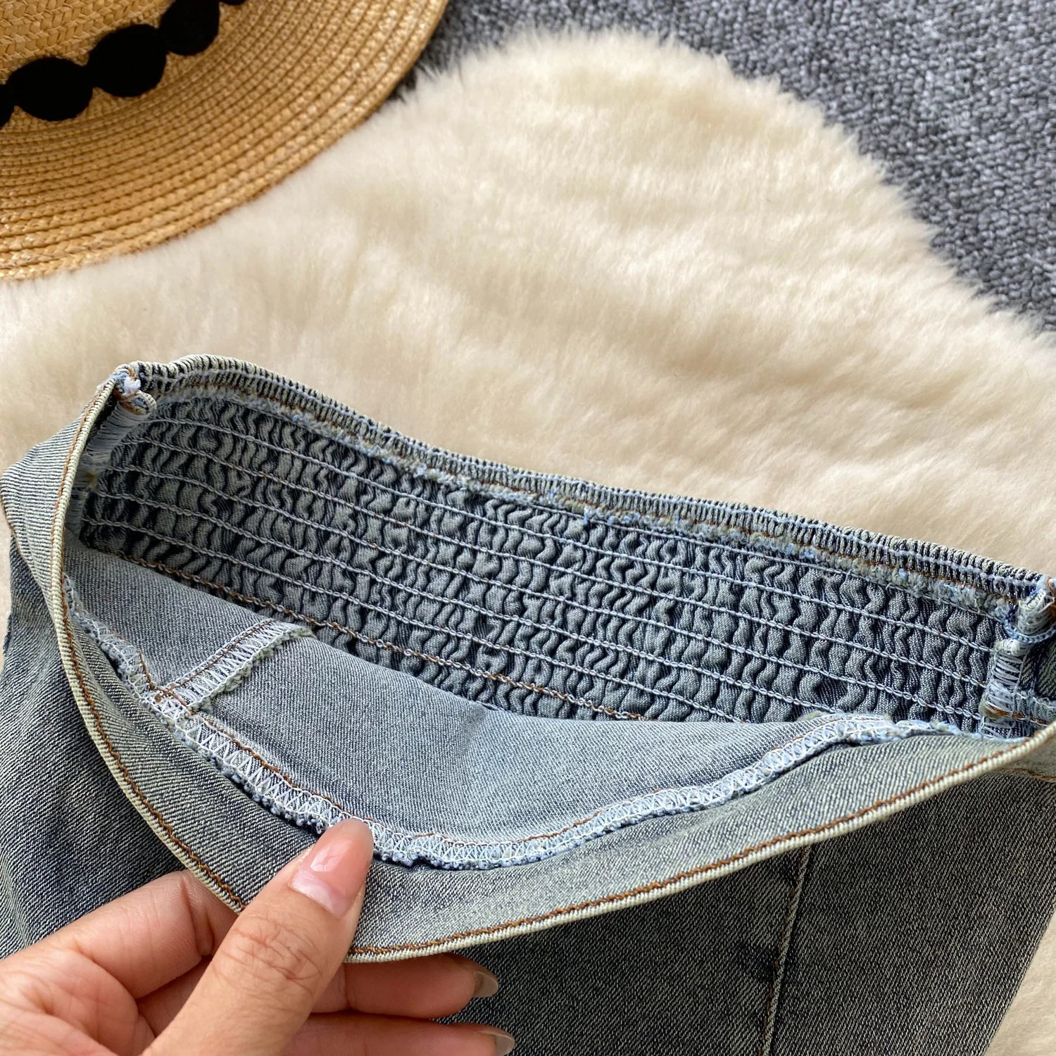 Close-up of a person holding a denim fabric with a textured pattern on a soft surface.