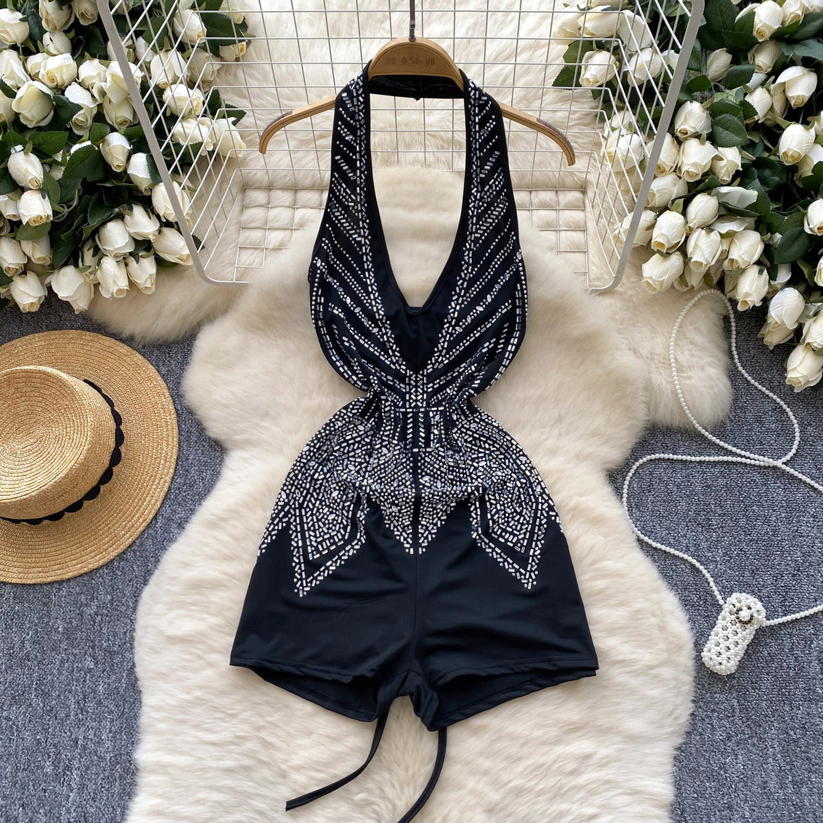 Black embellished romper on a hanger with decorative flowers and a hat in the background