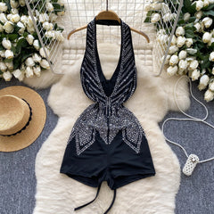Black embellished romper on a hanger with decorative flowers and a hat in the background