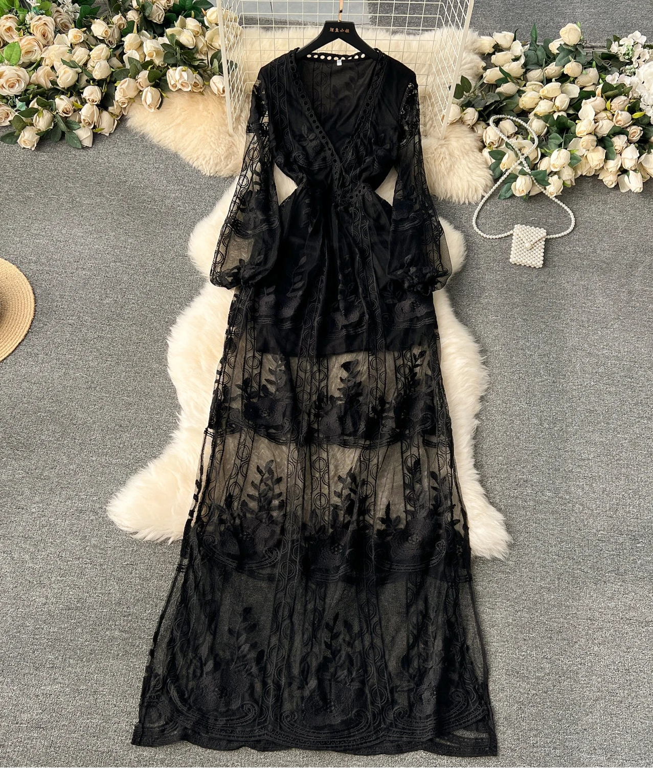 Black lace dress on a hanger with flowers and a hat in the background