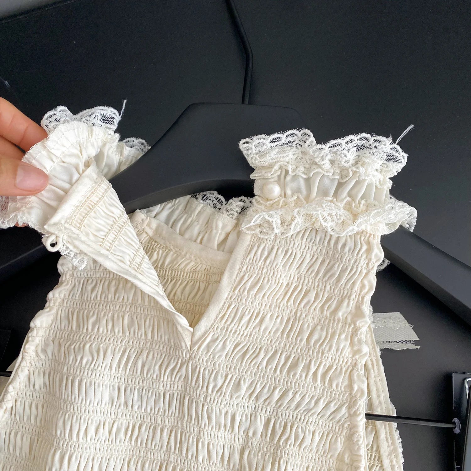 White lace-trimmed dress on a black hanger against a dark background