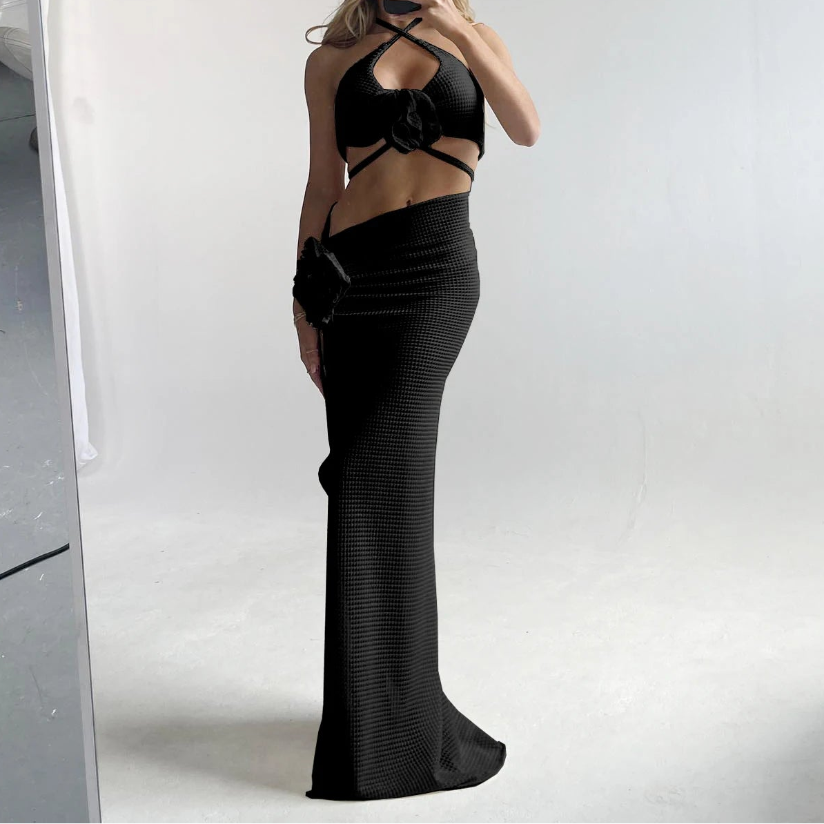 Person wearing a black dress with cut-out design and a white hat, standing in front of a mirror.