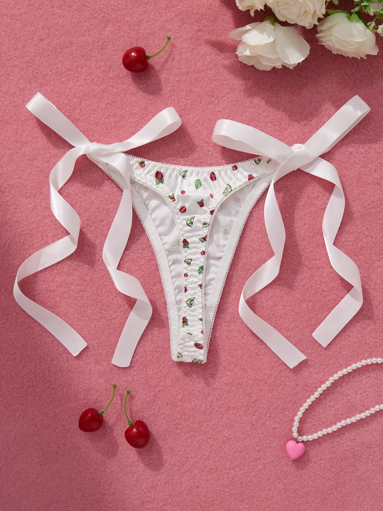 White lace thong with cherry pattern on a pink background with ribbons and cherries.