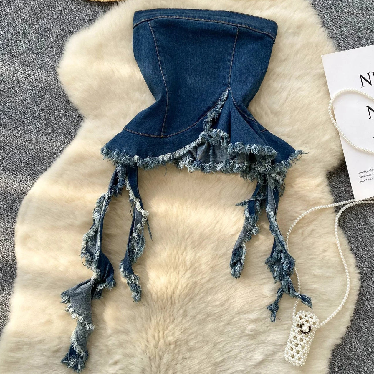 Denim bikini top with tassels on a fur surface with a hat and card in the background