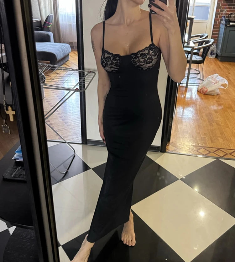 Woman taking a mirror selfie wearing a black lace dress in a room with checkered floor and furniture.