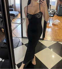 Woman taking a mirror selfie wearing a black lace dress in a room with checkered floor and furniture.