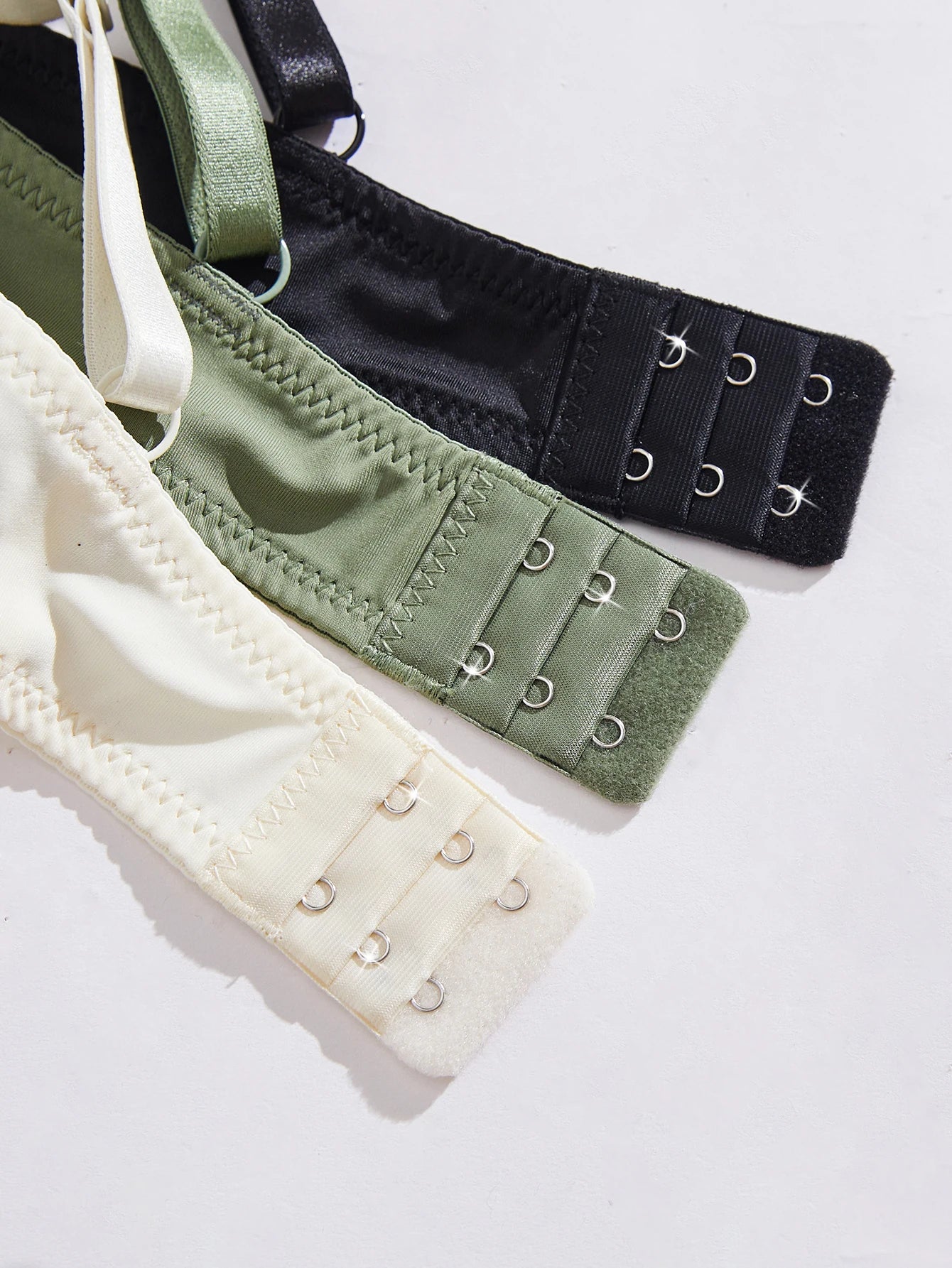 Three bra straps in black, green, and beige on a white background