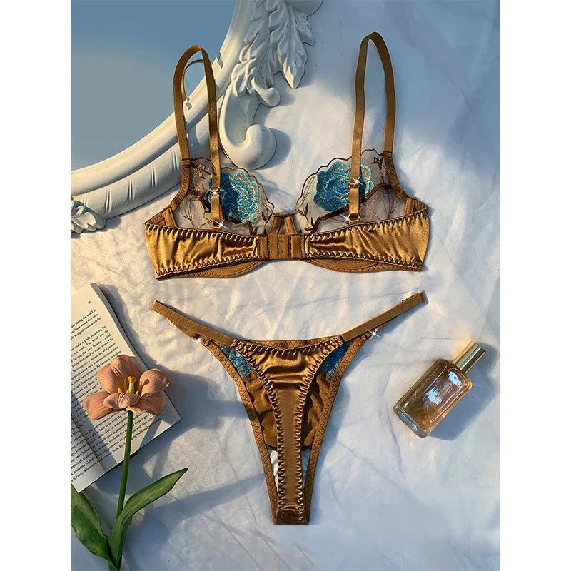 Gold bra set with floral details on a textured surface with a book and flower.