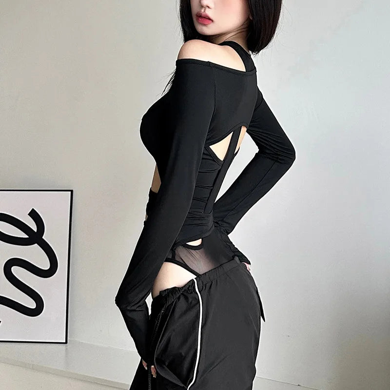 Person wearing a black long-sleeve top with cut-out design and black pants in a minimalistic setting.