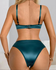 A woman shown from the back wearing a satin-like teal bikini bottom and matching bralette, with a light neutral indoor background.