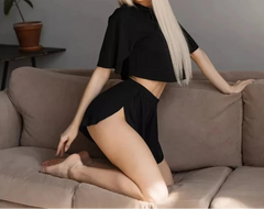 Woman in a black outfit sitting on a brown couch in a room with a plant.