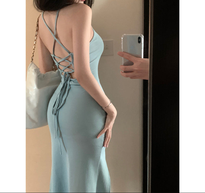 Woman in a light blue dress standing in front of a mirror, holding a phone.