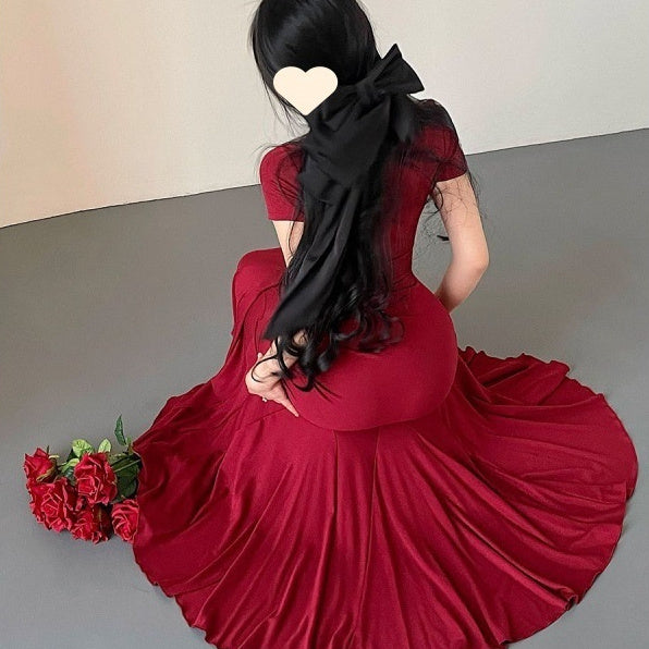 Woman in a red dress with a black scarf holding flowers on a plain background