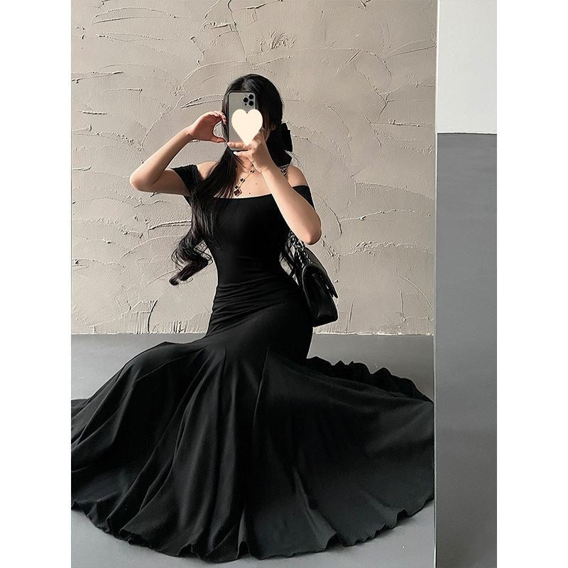 Woman in a black off-shoulder dress posing against a textured wall.