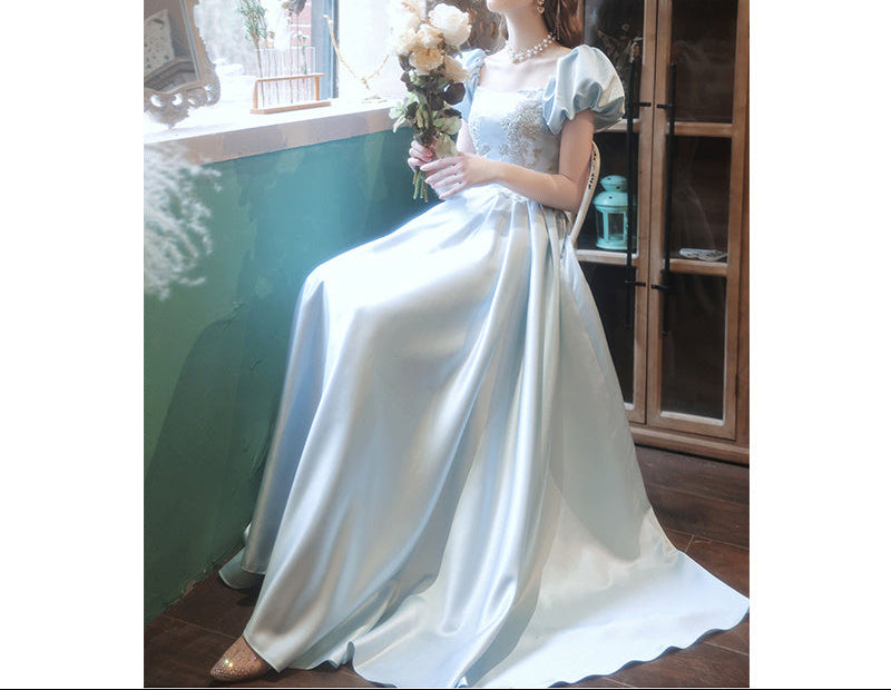 Woman in a white dress holding flowers by a window