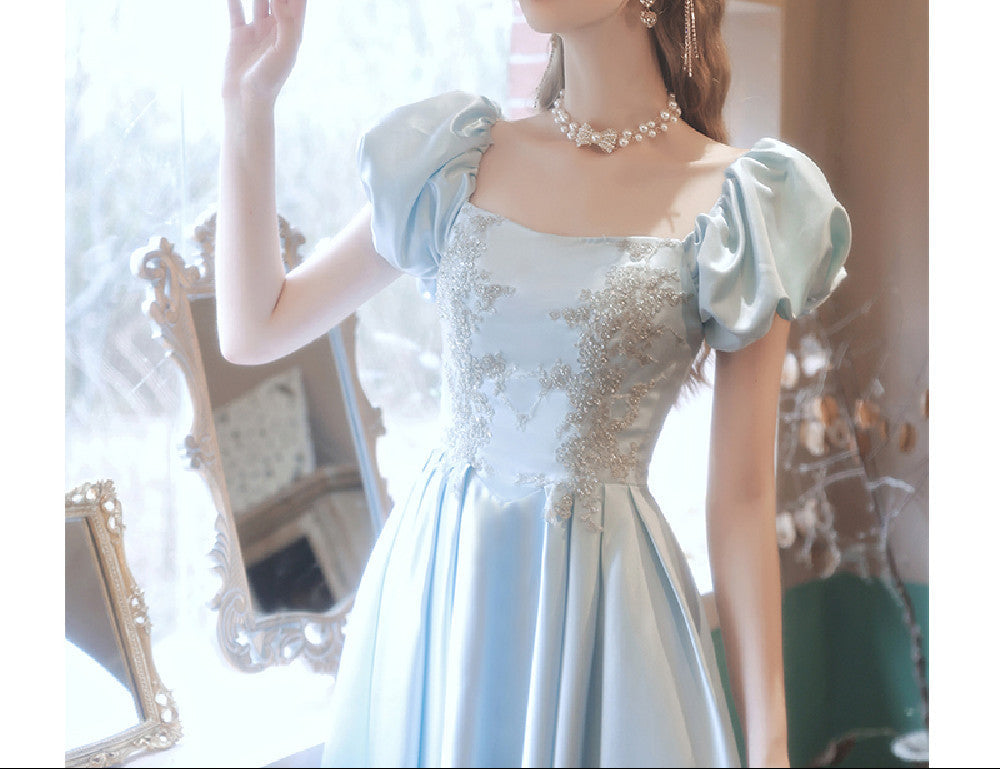 Woman in a light blue dress with floral details standing in a softly blurred room.