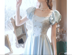 Woman in a light blue dress with floral details standing in a softly blurred room.