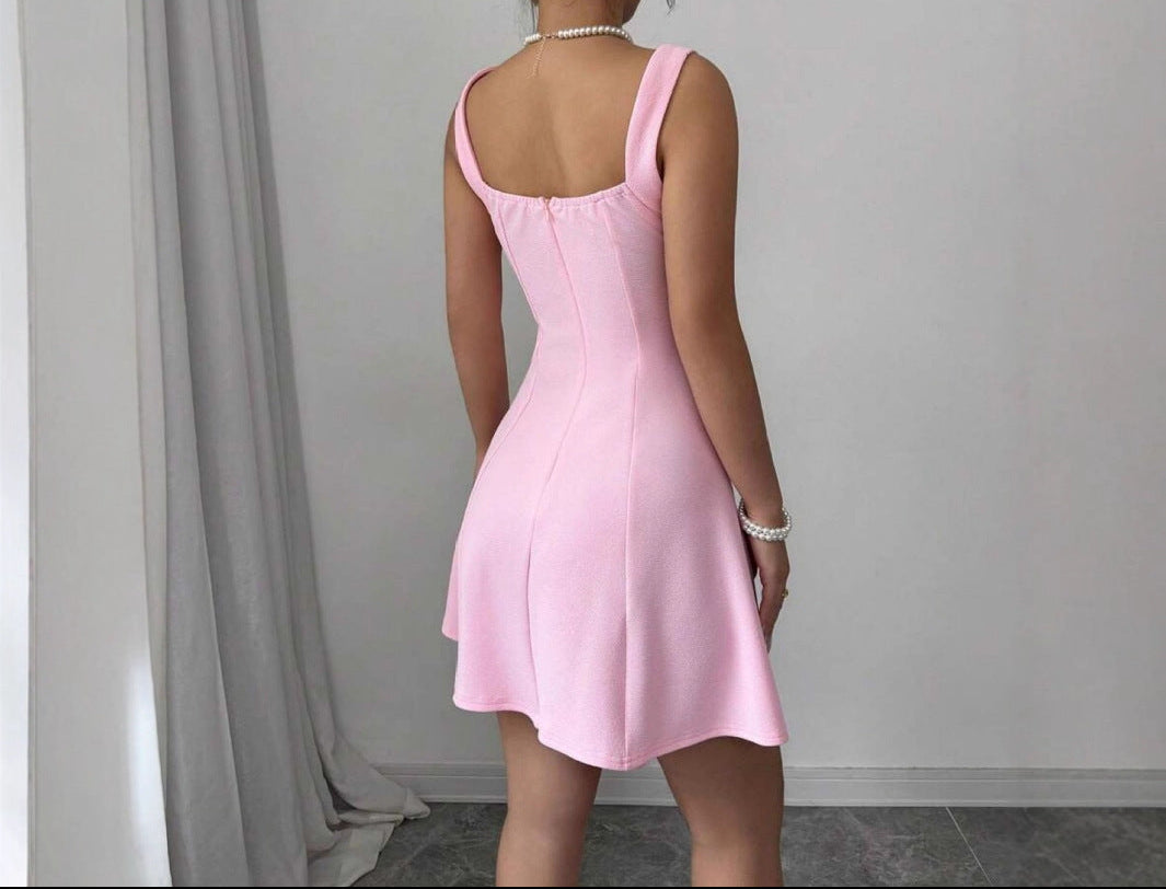 Person wearing a pink dress standing against a plain wall with gray curtains.